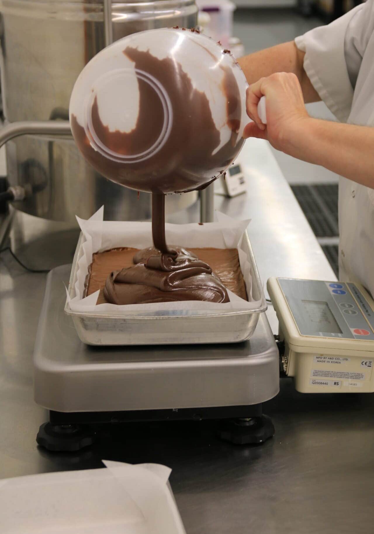 A maker pouring fudge in a pan on a scale